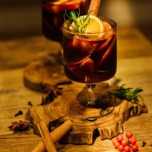 Close-up of festive mulled wine with cinnamon sticks and citrus slices on a wooden tray.